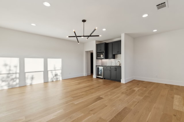 unfurnished living room featuring visible vents, light wood-style flooring, recessed lighting, wine cooler, and an inviting chandelier