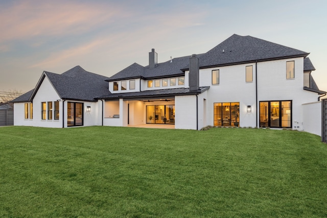 back of house featuring a lawn, a chimney, metal roof, a patio area, and a standing seam roof