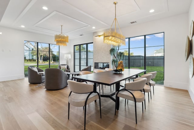 dining space with baseboards, a large fireplace, a chandelier, and light wood finished floors