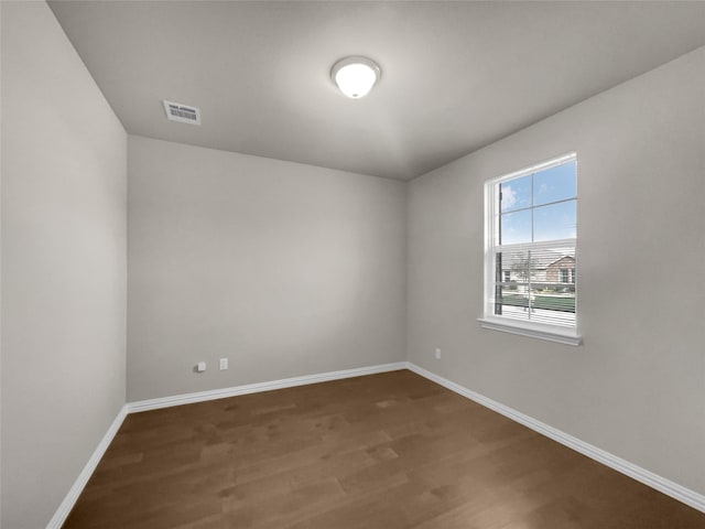 spare room with dark wood-type flooring, visible vents, and baseboards