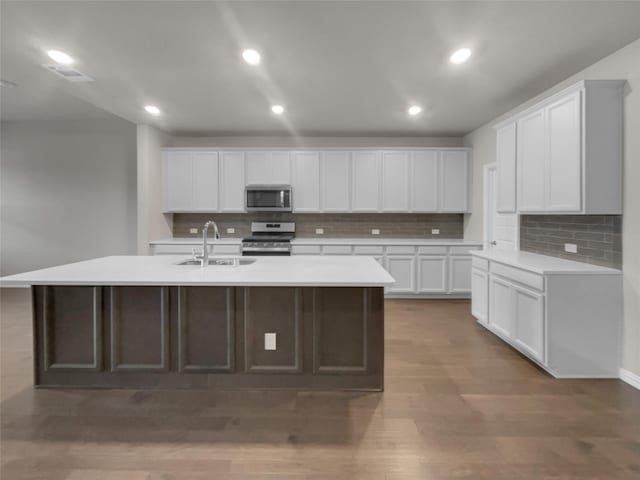 kitchen featuring a center island with sink, light countertops, appliances with stainless steel finishes, wood finished floors, and a sink