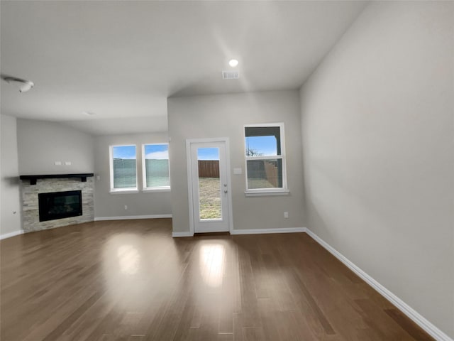 unfurnished living room with a glass covered fireplace, baseboards, visible vents, and dark wood-style flooring