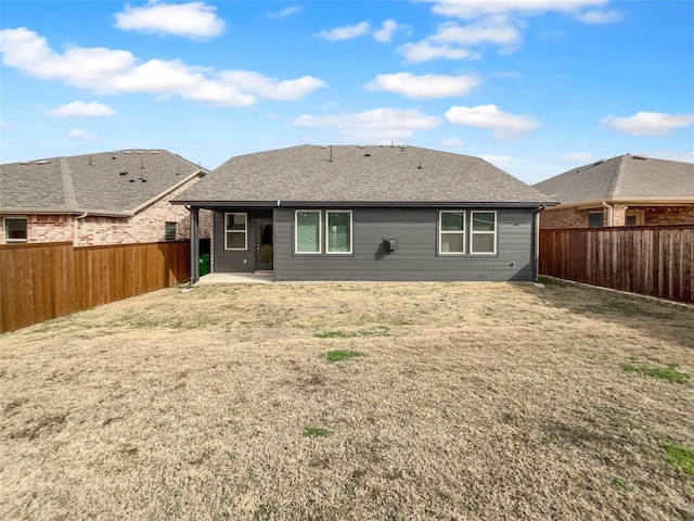 rear view of house featuring a patio area, a lawn, a shingled roof, and a fenced backyard