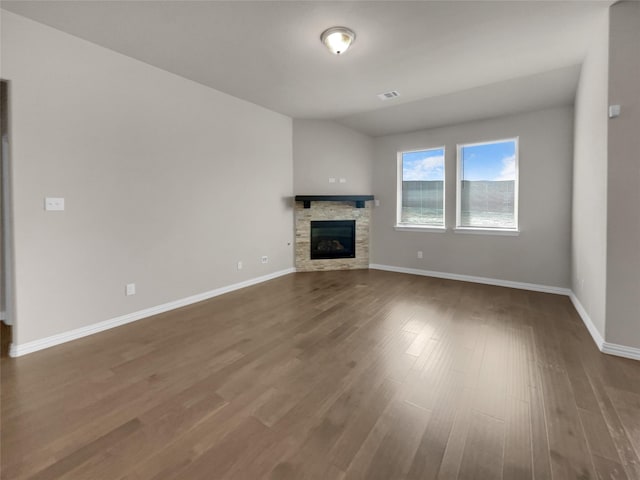 unfurnished living room with a stone fireplace, baseboards, visible vents, and wood finished floors