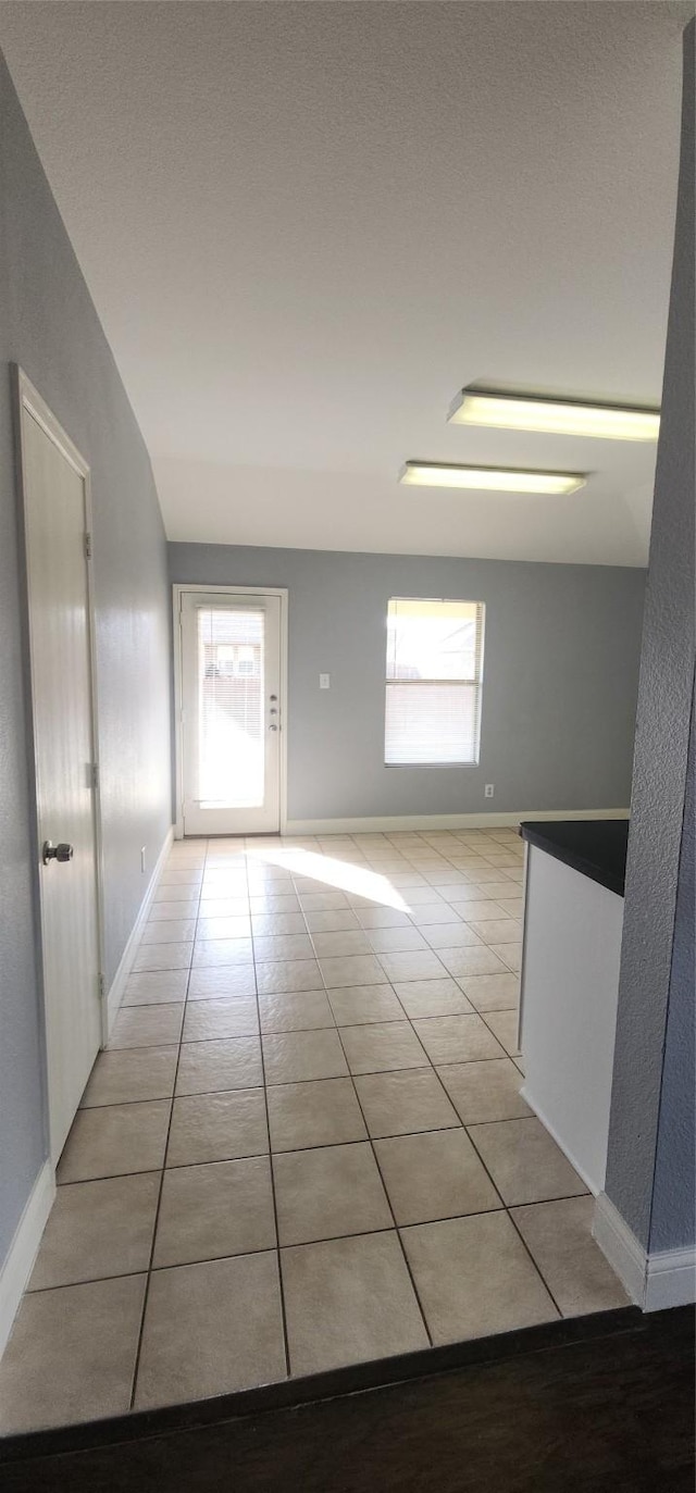 hall featuring a wealth of natural light, baseboards, and light tile patterned flooring