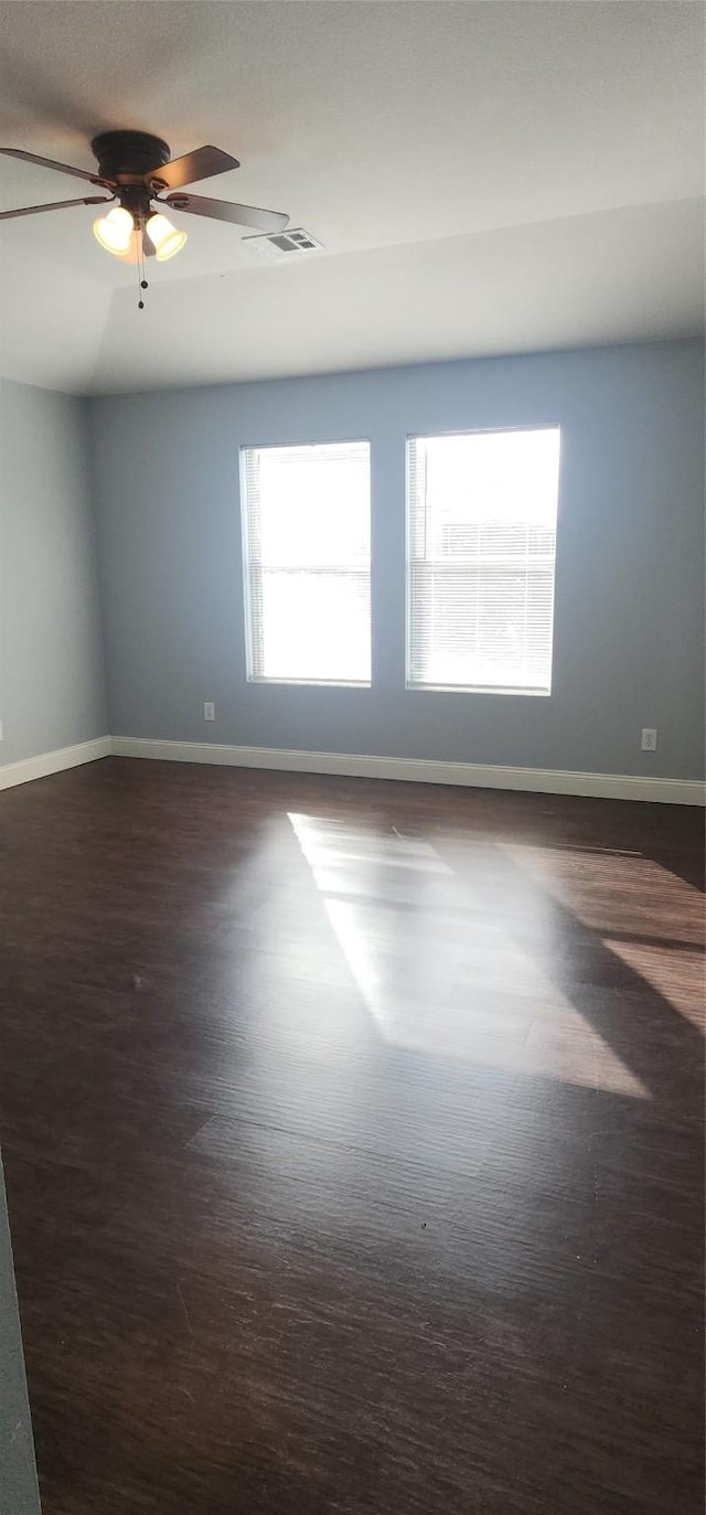 empty room featuring visible vents, a ceiling fan, baseboards, and dark wood-style flooring