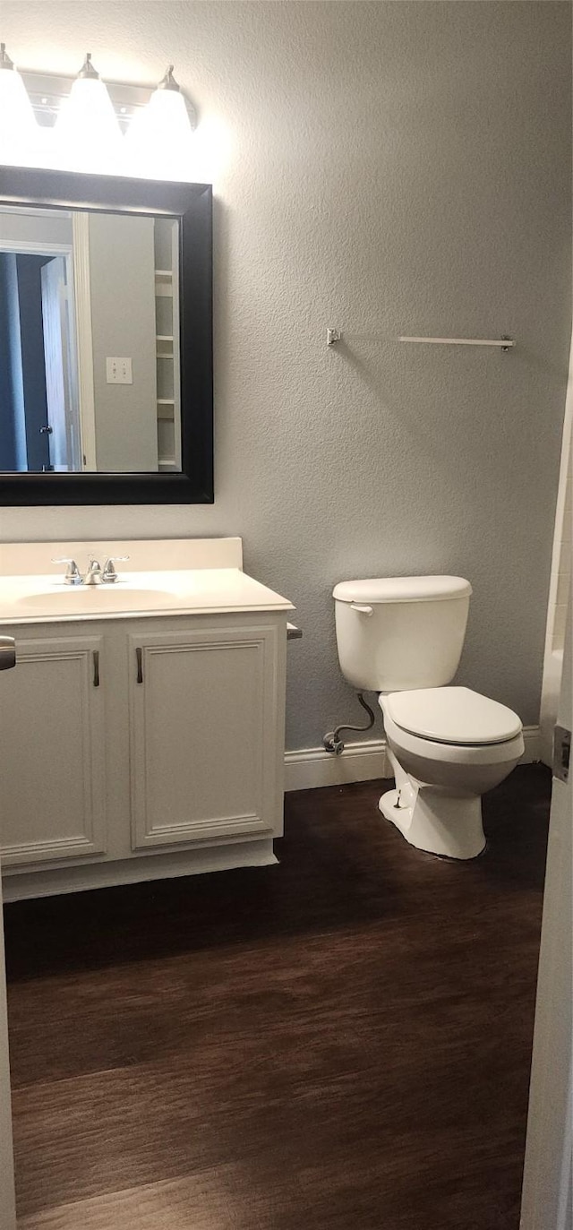 bathroom featuring baseboards, toilet, wood finished floors, and vanity