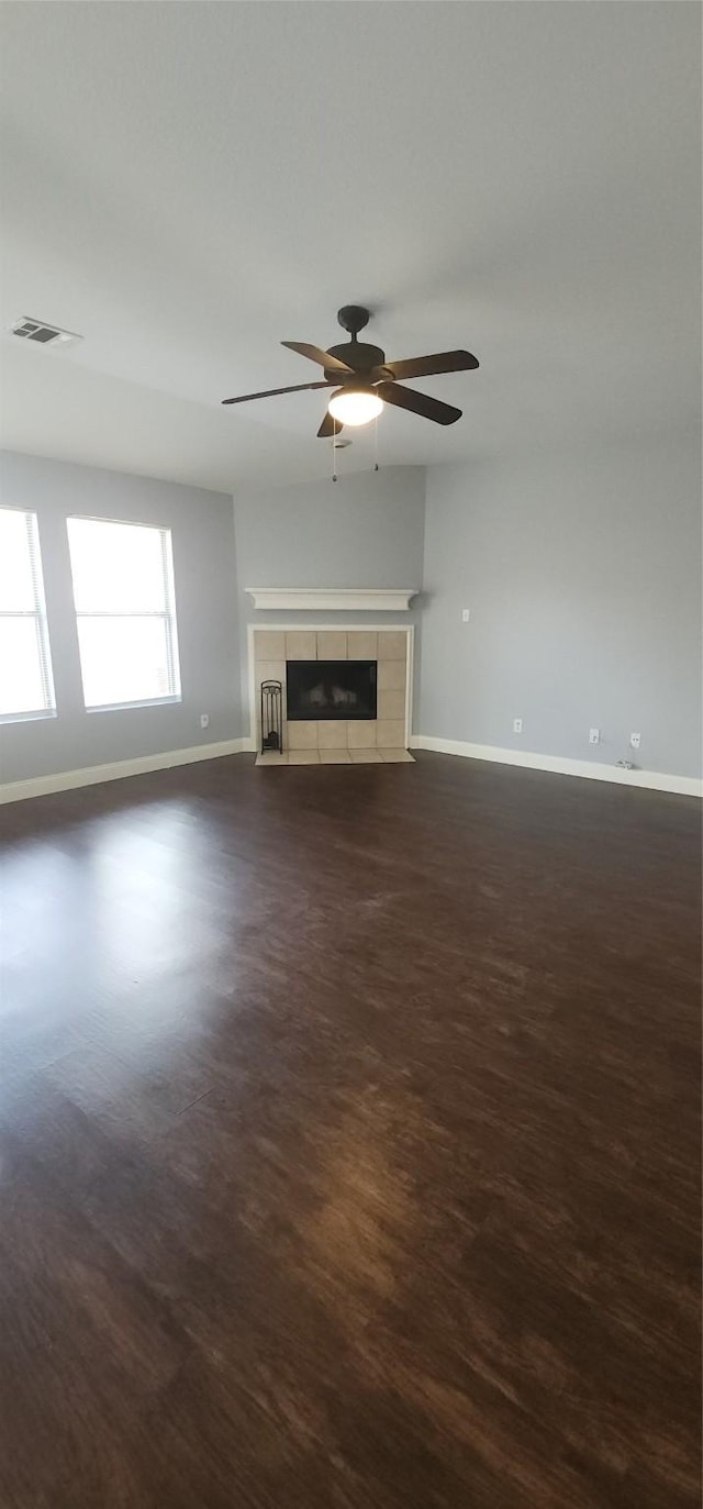 unfurnished living room with a ceiling fan, baseboards, visible vents, dark wood finished floors, and a tiled fireplace