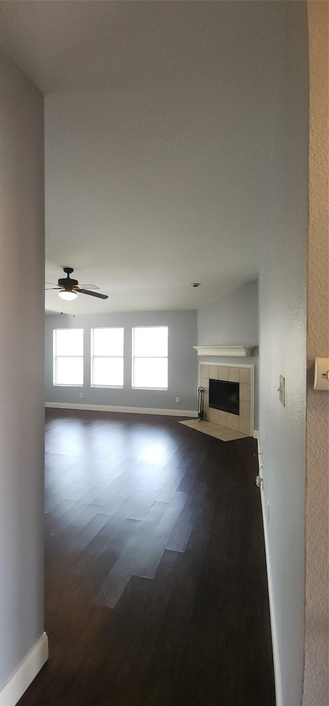 unfurnished living room featuring plenty of natural light, a tile fireplace, dark wood-type flooring, and baseboards