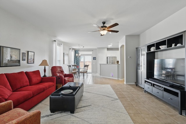 living area with light tile patterned floors, baseboards, arched walkways, and a ceiling fan