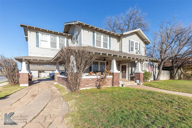 view of front of house with brick siding, ceiling fan, concrete driveway, a front yard, and covered porch