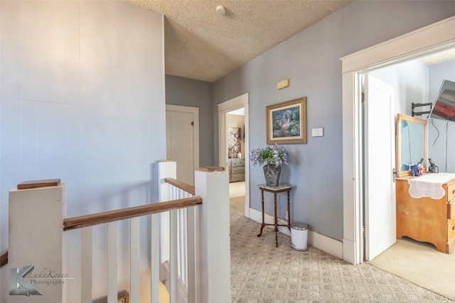 corridor featuring baseboards, an upstairs landing, carpet, and a textured ceiling