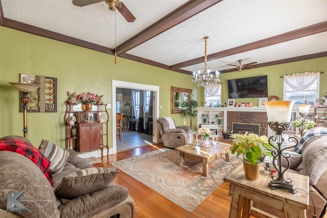 living area with wood finished floors, beam ceiling, a fireplace, a textured ceiling, and ceiling fan with notable chandelier