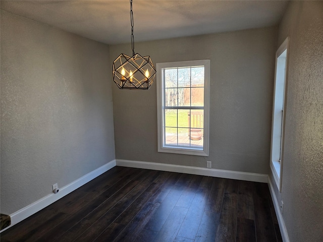 empty room with dark wood-style floors, a chandelier, baseboards, and a textured wall