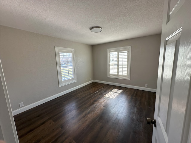 unfurnished bedroom featuring multiple windows, baseboards, dark wood-style flooring, and a textured ceiling