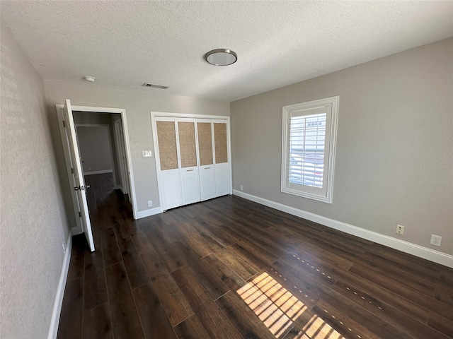 unfurnished bedroom featuring visible vents, baseboards, a textured ceiling, and dark wood finished floors