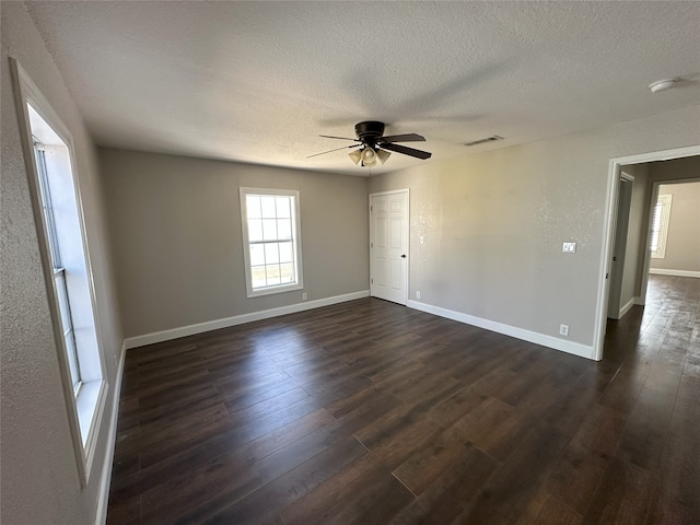 spare room featuring visible vents, baseboards, a textured ceiling, and dark wood-style floors