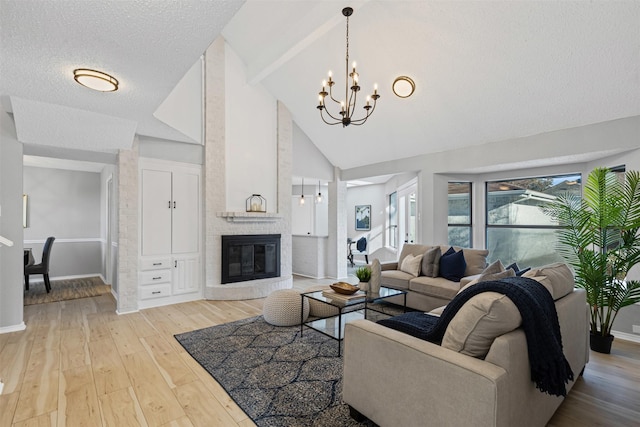 living area with high vaulted ceiling, light wood finished floors, baseboards, a brick fireplace, and a chandelier