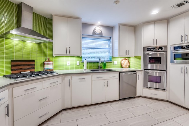 kitchen with visible vents, a sink, appliances with stainless steel finishes, wall chimney exhaust hood, and tasteful backsplash