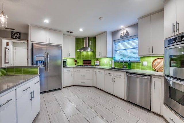 kitchen featuring visible vents, appliances with stainless steel finishes, white cabinetry, wall chimney exhaust hood, and a sink