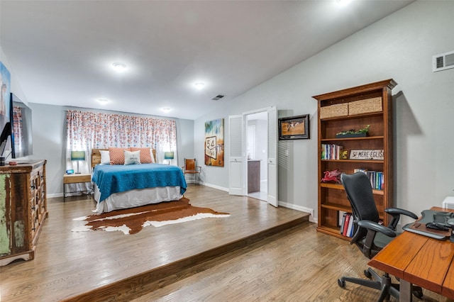 bedroom with lofted ceiling, wood finished floors, visible vents, and baseboards