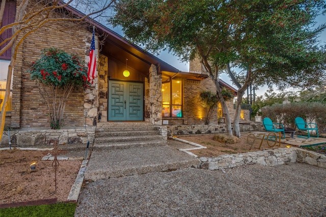 property entrance featuring a patio area, stone siding, and a chimney