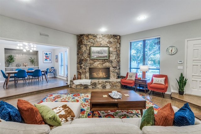 living room featuring a stone fireplace, wood finished floors, visible vents, and a chandelier