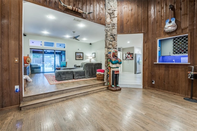 living room featuring ceiling fan, a bar, wood finished floors, and wooden walls