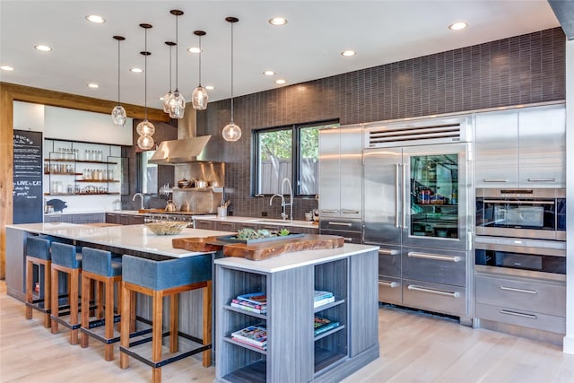 kitchen featuring light wood-style flooring, open shelves, tasteful backsplash, wall chimney exhaust hood, and light countertops