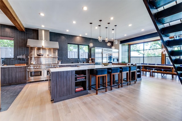 kitchen with range with two ovens, light countertops, beamed ceiling, wall chimney exhaust hood, and modern cabinets