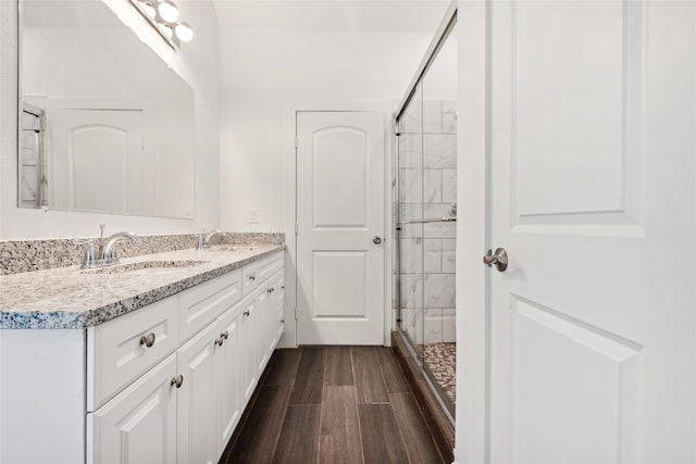 full bathroom with a sink, wood finish floors, double vanity, and a tile shower