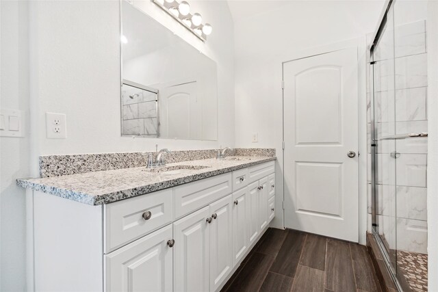 bathroom featuring a sink, wood finish floors, a stall shower, and double vanity