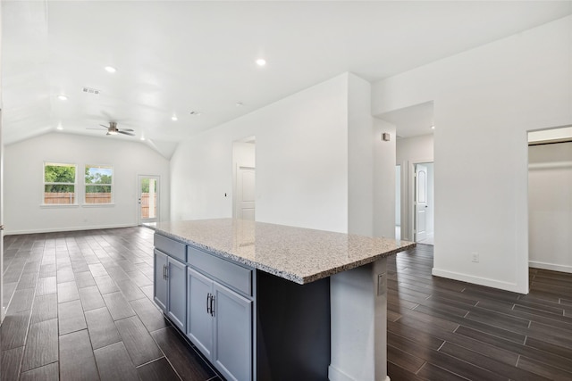 kitchen with a kitchen island, wood tiled floor, open floor plan, vaulted ceiling, and light stone counters