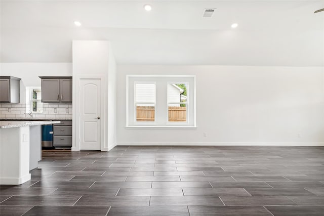 unfurnished living room with plenty of natural light, visible vents, lofted ceiling, and wood finish floors