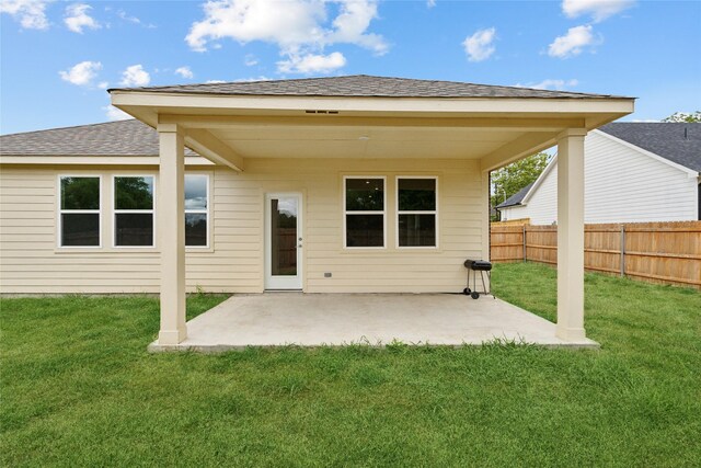 back of property with a patio area, roof with shingles, a yard, and fence