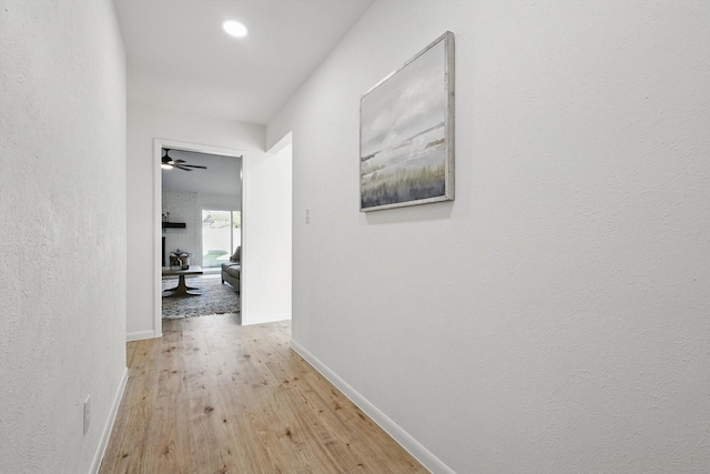 hallway with baseboards, wood finished floors, and a textured wall