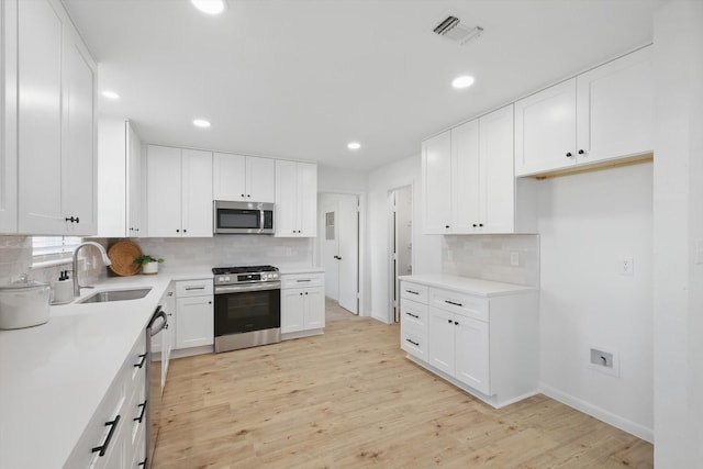 kitchen featuring light wood finished floors, visible vents, white cabinets, stainless steel appliances, and a sink