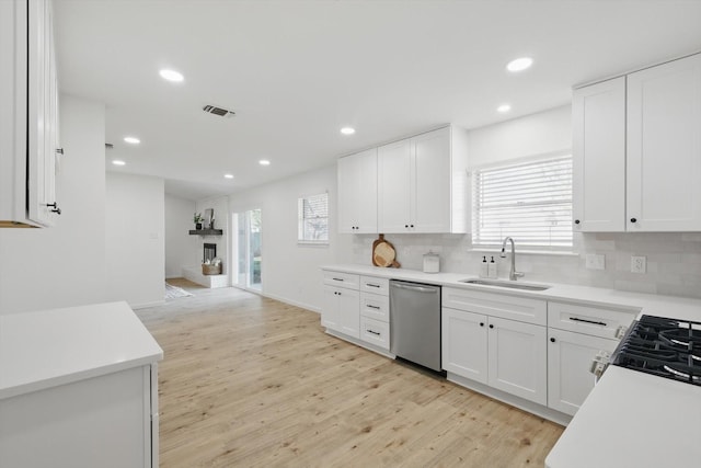 kitchen featuring light wood-type flooring, a sink, tasteful backsplash, a large fireplace, and dishwasher