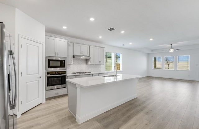 kitchen featuring visible vents, under cabinet range hood, a sink, stainless steel appliances, and light wood-style floors