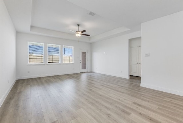 empty room featuring a tray ceiling, baseboards, ceiling fan, and light wood finished floors