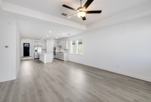 unfurnished living room with a tray ceiling, visible vents, baseboards, and light wood-style floors