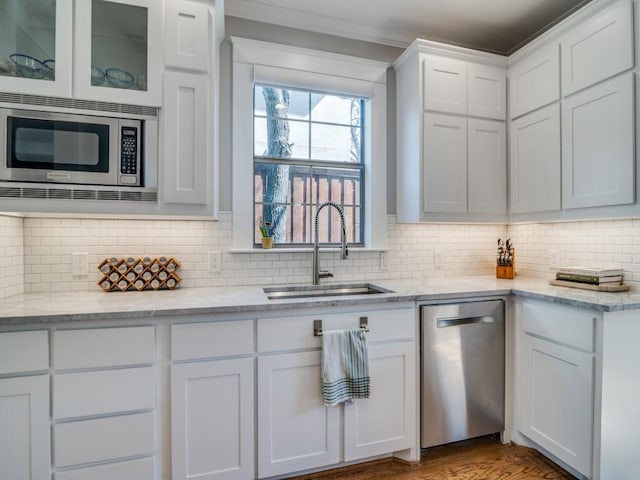 kitchen featuring tasteful backsplash, stainless steel appliances, wood finished floors, white cabinetry, and a sink