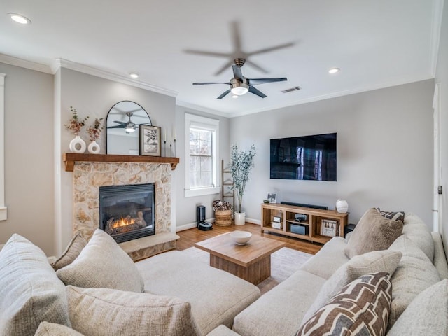 living area with visible vents, ornamental molding, wood finished floors, a stone fireplace, and baseboards