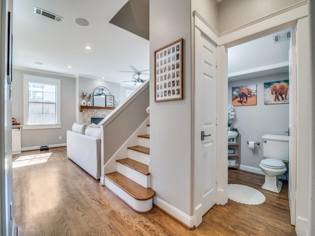 stairs with visible vents, baseboards, ornamental molding, a stone fireplace, and wood finished floors