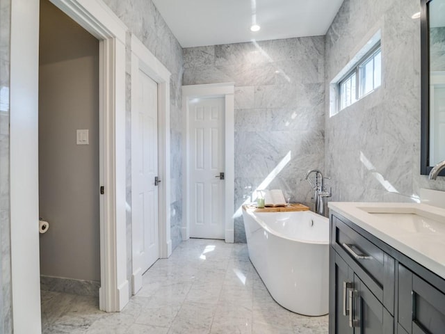 bathroom featuring tile walls, a freestanding bath, marble finish floor, and vanity