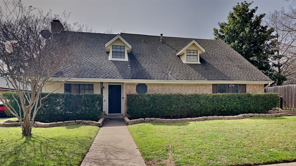 view of front of home with brick siding, roof with shingles, a front yard, and fence