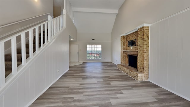 unfurnished living room featuring beamed ceiling, high vaulted ceiling, wood finished floors, stairway, and a brick fireplace