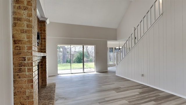 unfurnished living room featuring light wood finished floors, stairway, a fireplace, a notable chandelier, and high vaulted ceiling