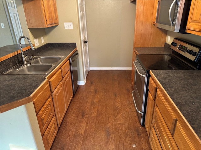 kitchen with dark countertops, dark wood-style flooring, appliances with stainless steel finishes, and a sink