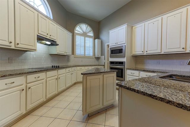 kitchen with a sink, under cabinet range hood, stainless steel appliances, light tile patterned flooring, and decorative backsplash